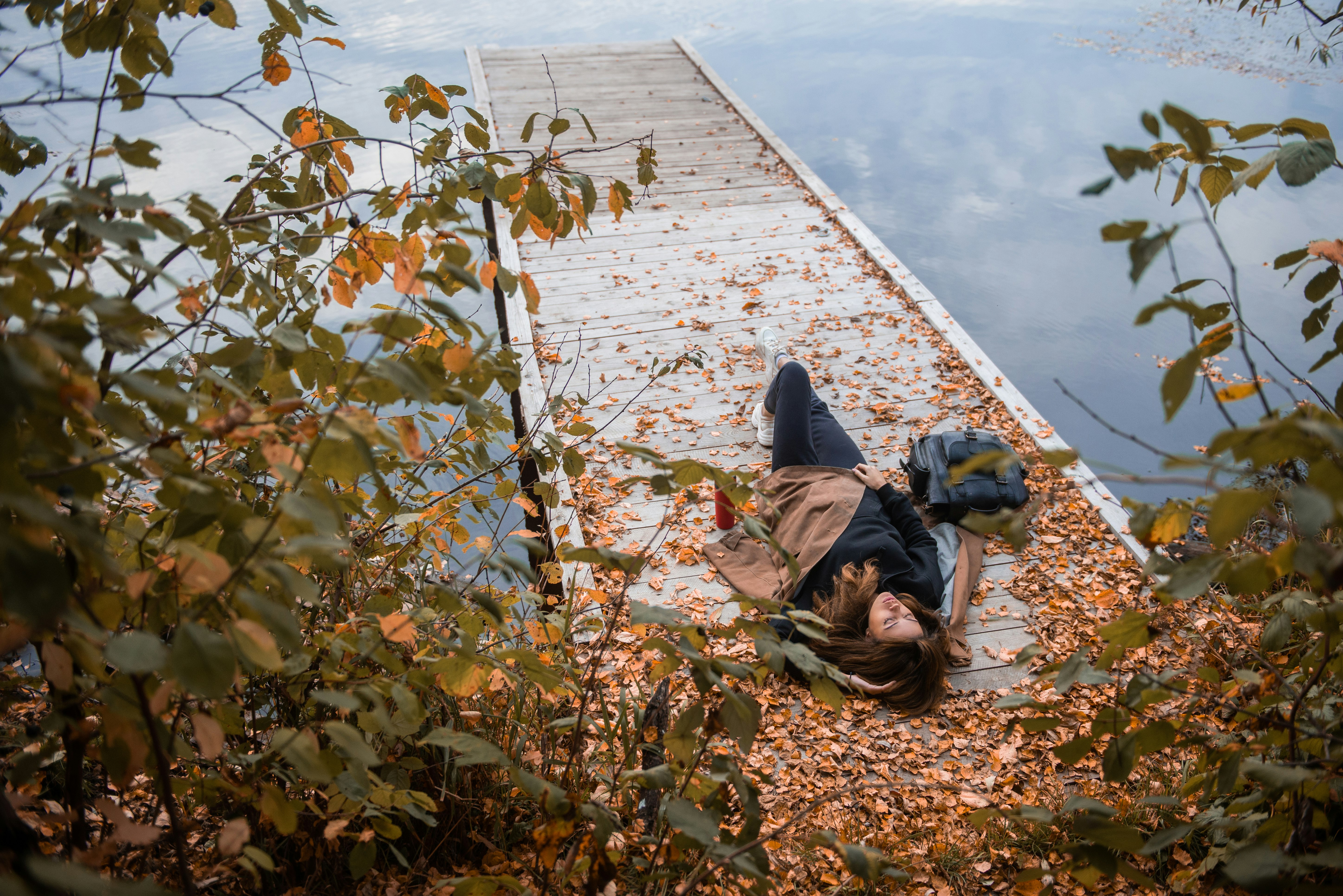 person in black jacket lying on brown wooden dock during daytime